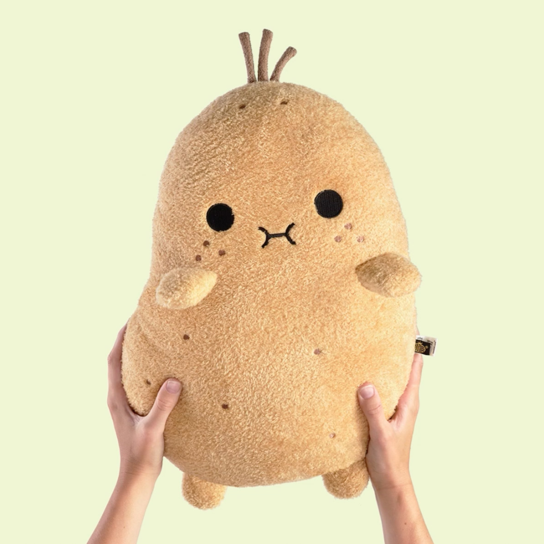 Person holding Snug Spud™ plushie from Fluffy Haven, ultra-soft kawaii potato toy in hands against light green background